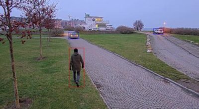 Camera view of a person walking along a driveway, detected by AXIS Object Analytics and highlighted within a bounding box.